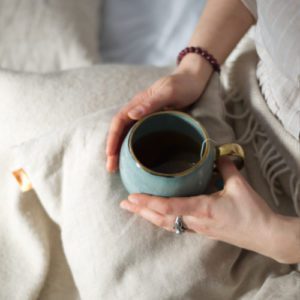 a woman holding a cup of tea on a husk pillow over her lap