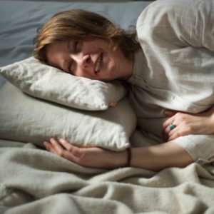 a woman lying happily in bed on two husk pillows